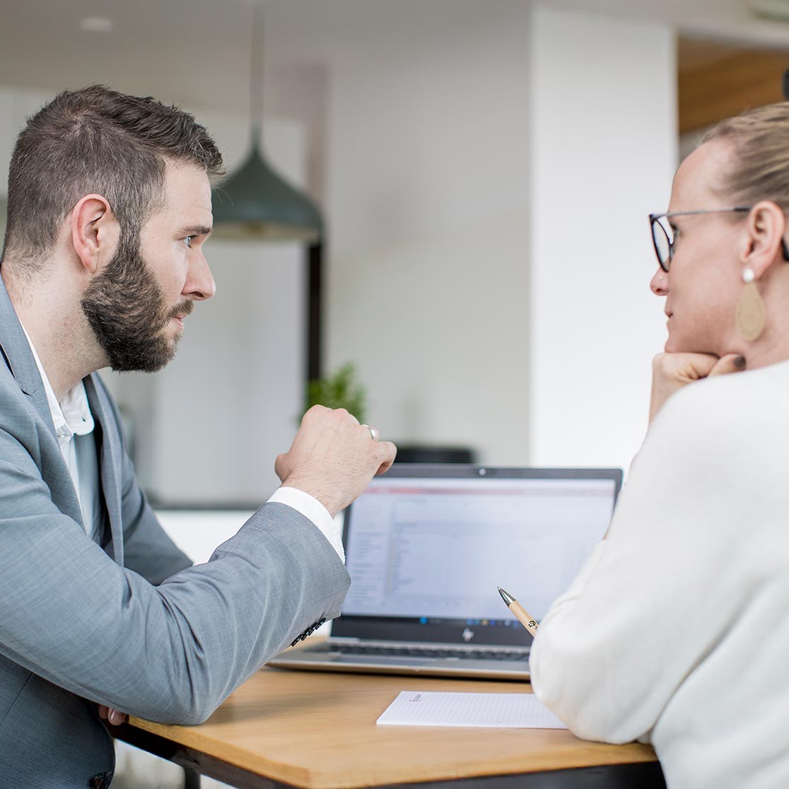 Ein Mann im Anzug und eine Frau vor einem Laptop.