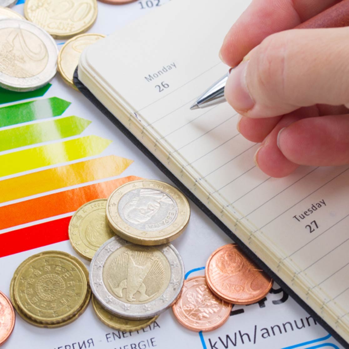 Eine Hand mit Kugelschreiber auf einem Notizbuch, umgeben von Kleingeld.