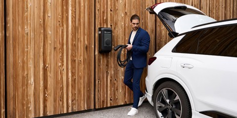 Mann lädt E-Auto an Wallbox vor Holzhintergrund.