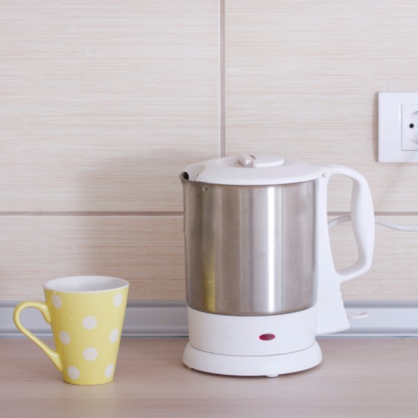 Electrical kettle and yellow dotted teacup on kitchen countertop