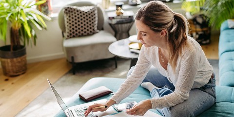 Frau sitzt auf Couch und arbeitet am Laptop.