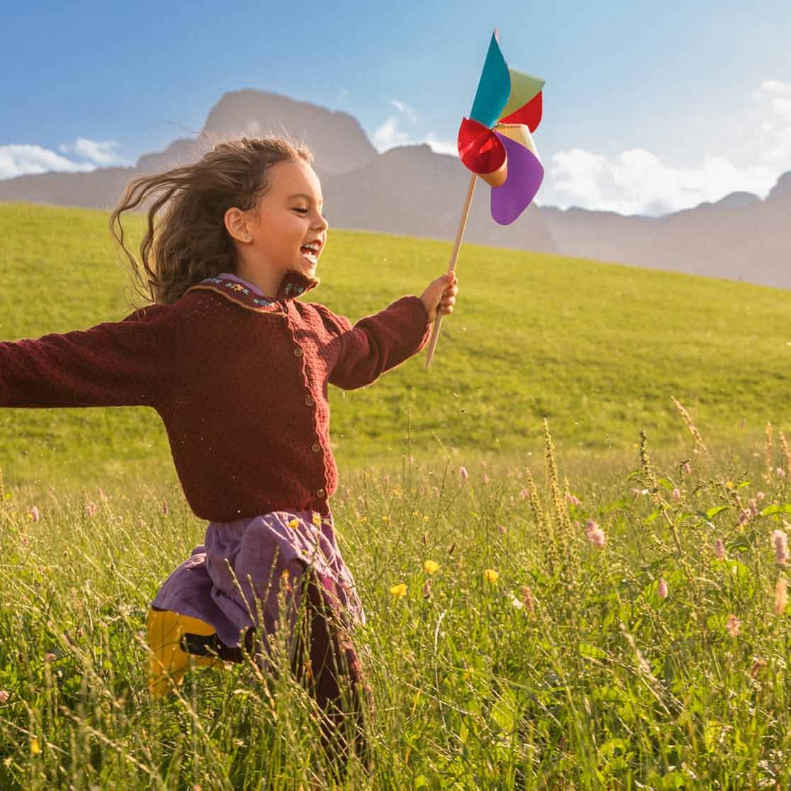Mädchen läuft mit Windrad in der Hand über Wiese.