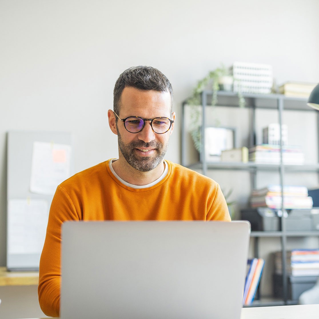 Geschäftsmann in lockeren Klamotten und Brille sitzt im Büro an seinem Schreibtisch vor seinem Laptop
