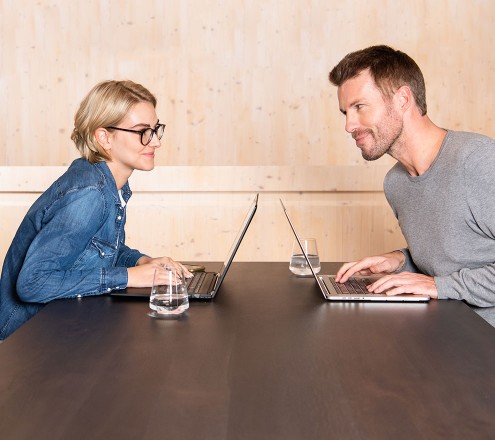 Mann und Frau arbeiten gemeinsam an Laptops gegenüber und schauen sich an.