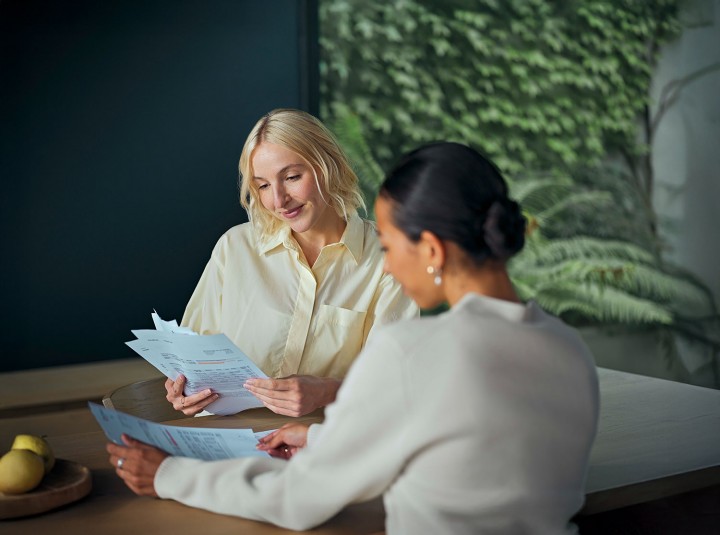 Zwei Personen sitzen an einem Tisch und besprechen Dokumente, im Hintergrund grüne Pflanzenwand.