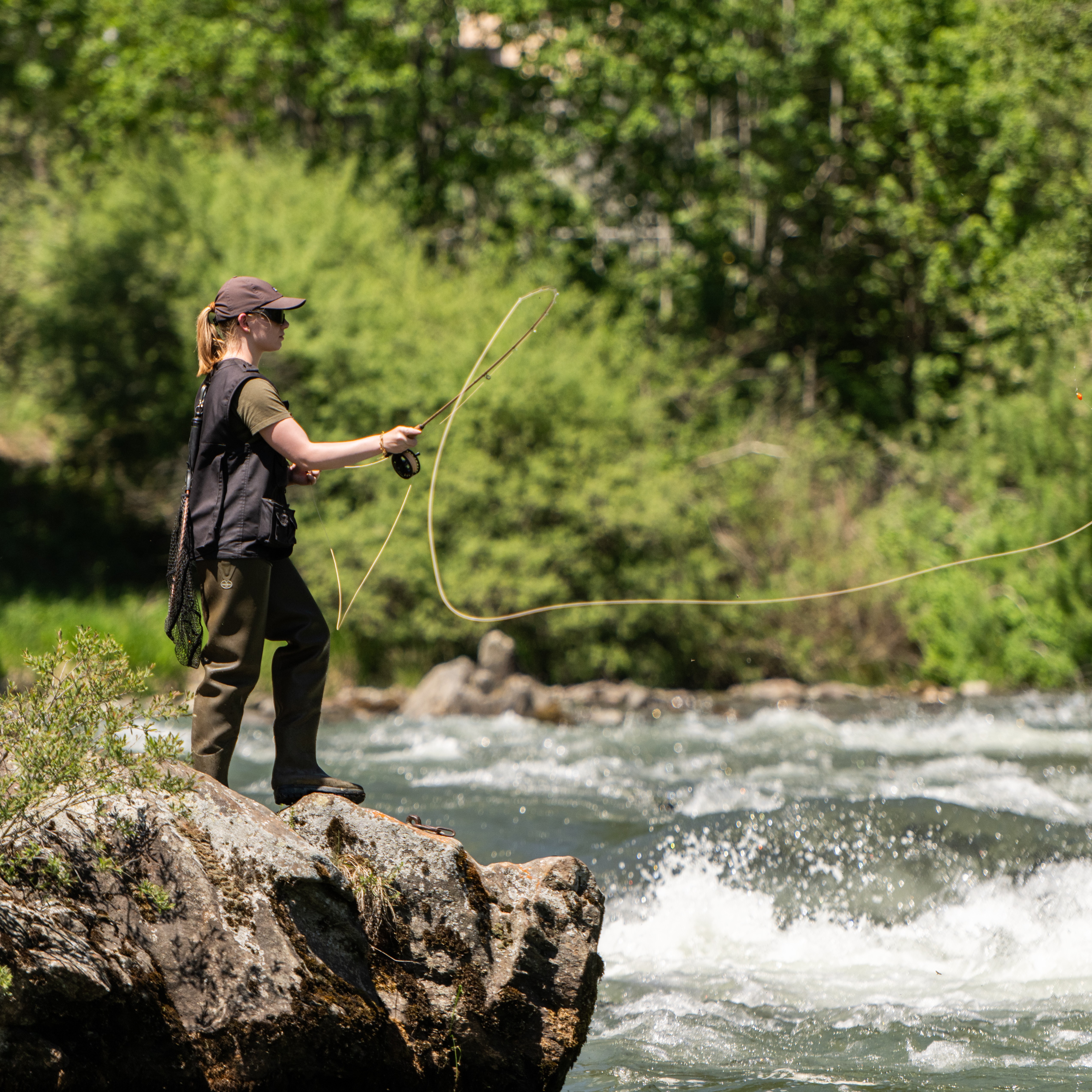 Eine Frau steht an einem Fluss und wirft eine Angel aus
